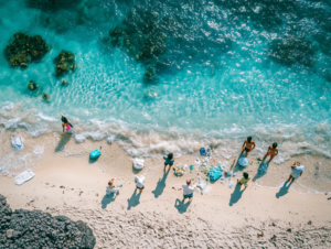 A diverse group of travelers collecting plastic waste on a Bali beach, using biodegradable bags and wearing reef-safe sunscreen. Crystal-clear turquoise water contrasts with the pollution being removed. Inspiring community action, documentary-style photography with vibrant colors.